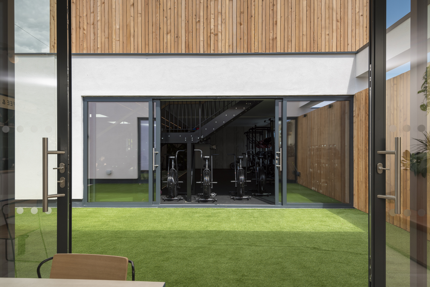 Looking through two sets of open bifold doors into a room filled with modern gym equipment