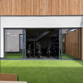 Looking through two sets of open bifold doors into a room filled with modern gym equipment
