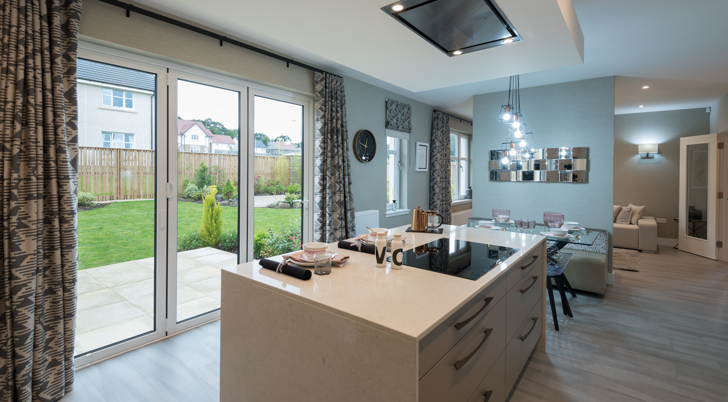 A modern kitchen looking out through closed bifold doors into a garden