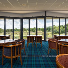 Inside a golf club with chairs and tables looking out onto the course through closed Origin bifold doors