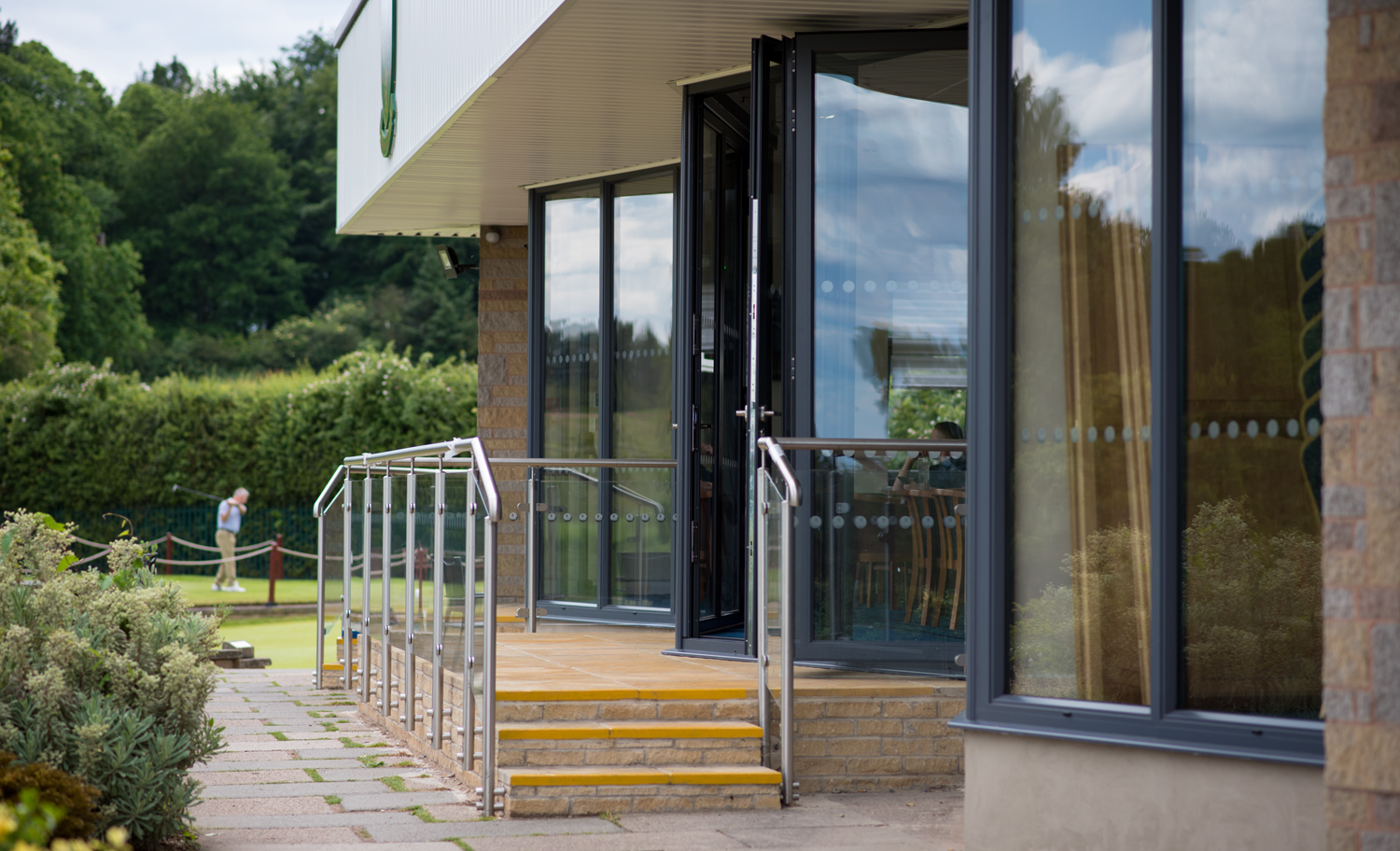 Golf club bifold doors viewed from the side with golfers in the background