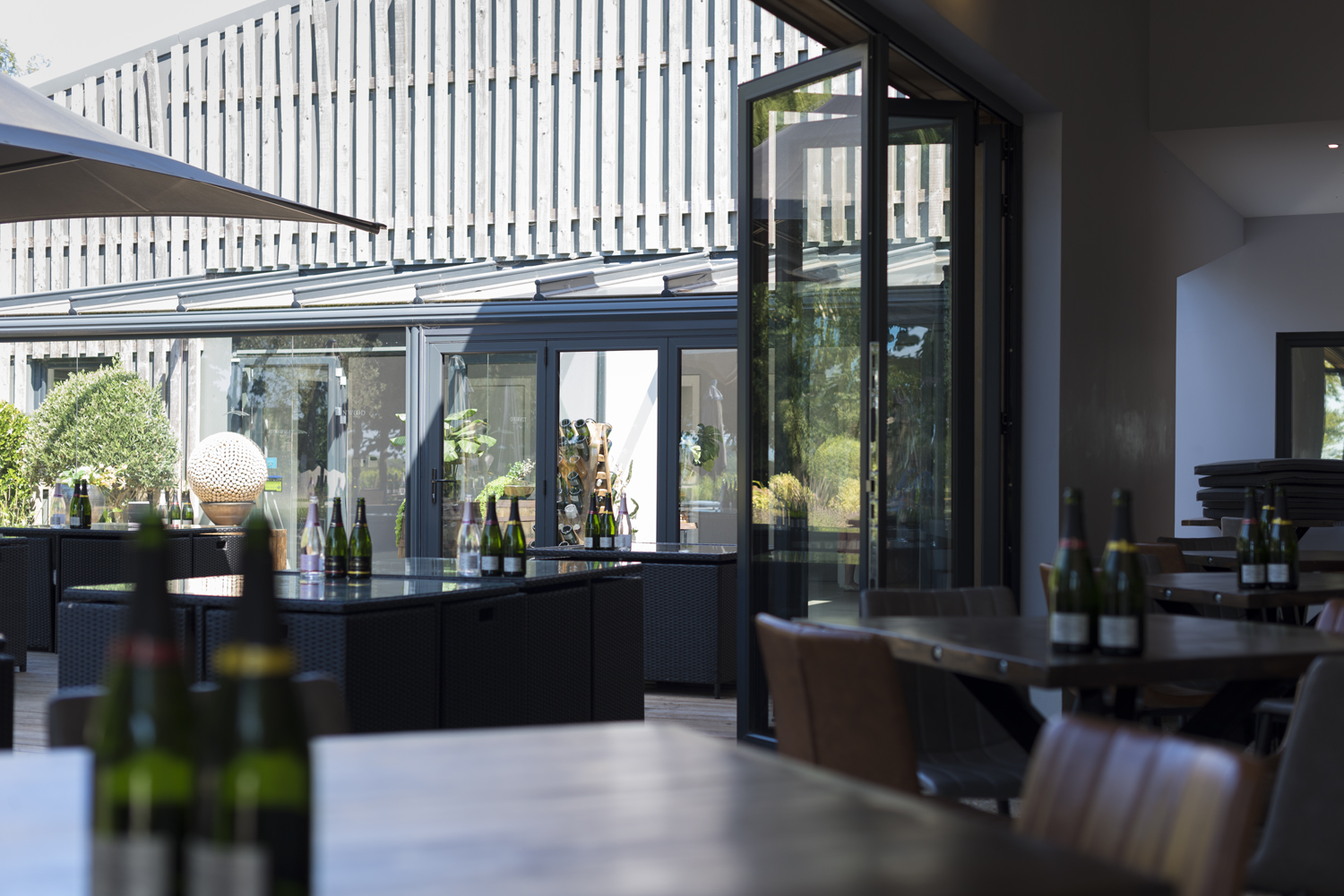 Inside of a bar viewing through open bifold doors into the garden with bottles on tables