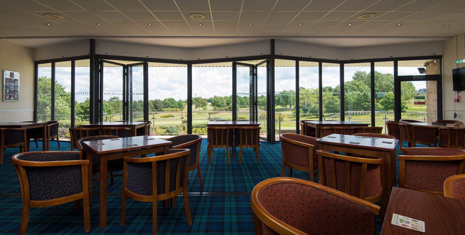 Inside a golf club with chairs and tables looking out onto the course through half open Origin bifold doors