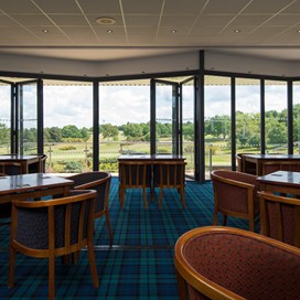 Inside a golf club with chairs and tables looking out onto the course through half open Origin bifold doors