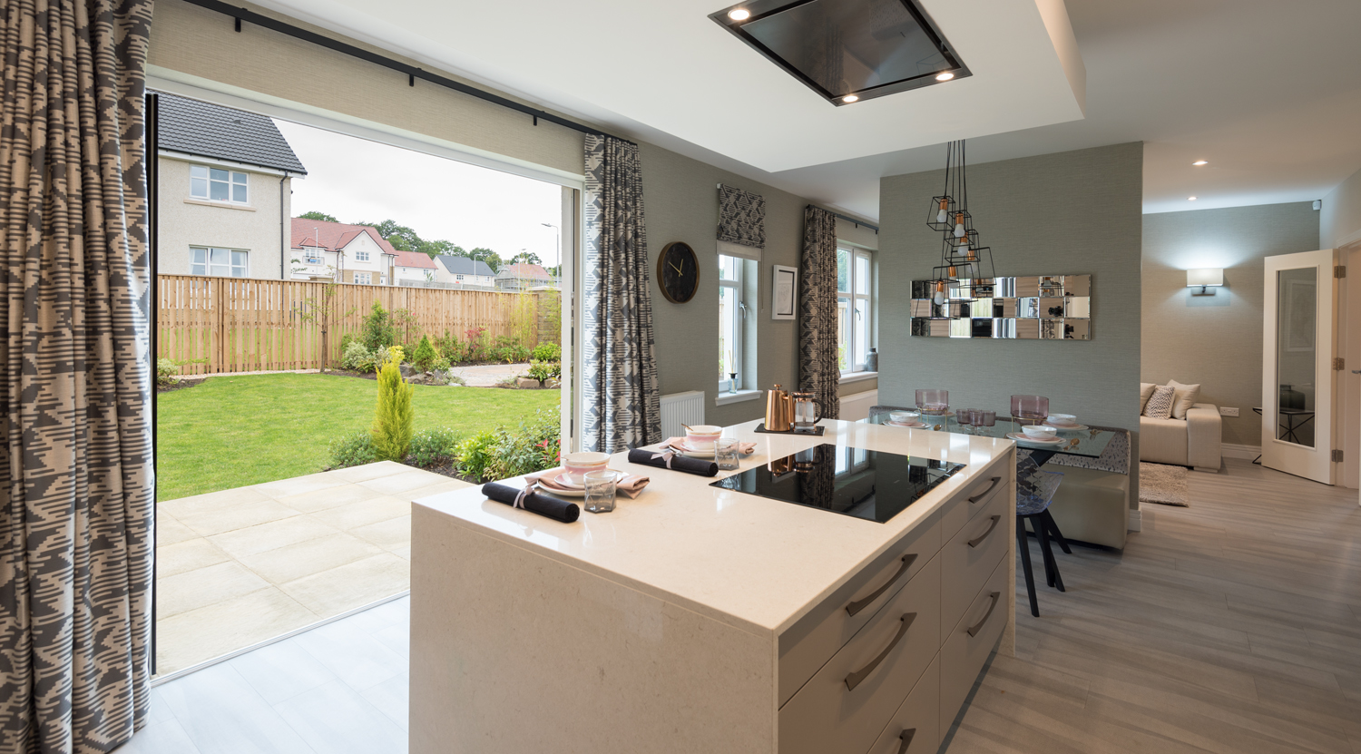 A modern kitchen looking out through open bifold doors into a garden