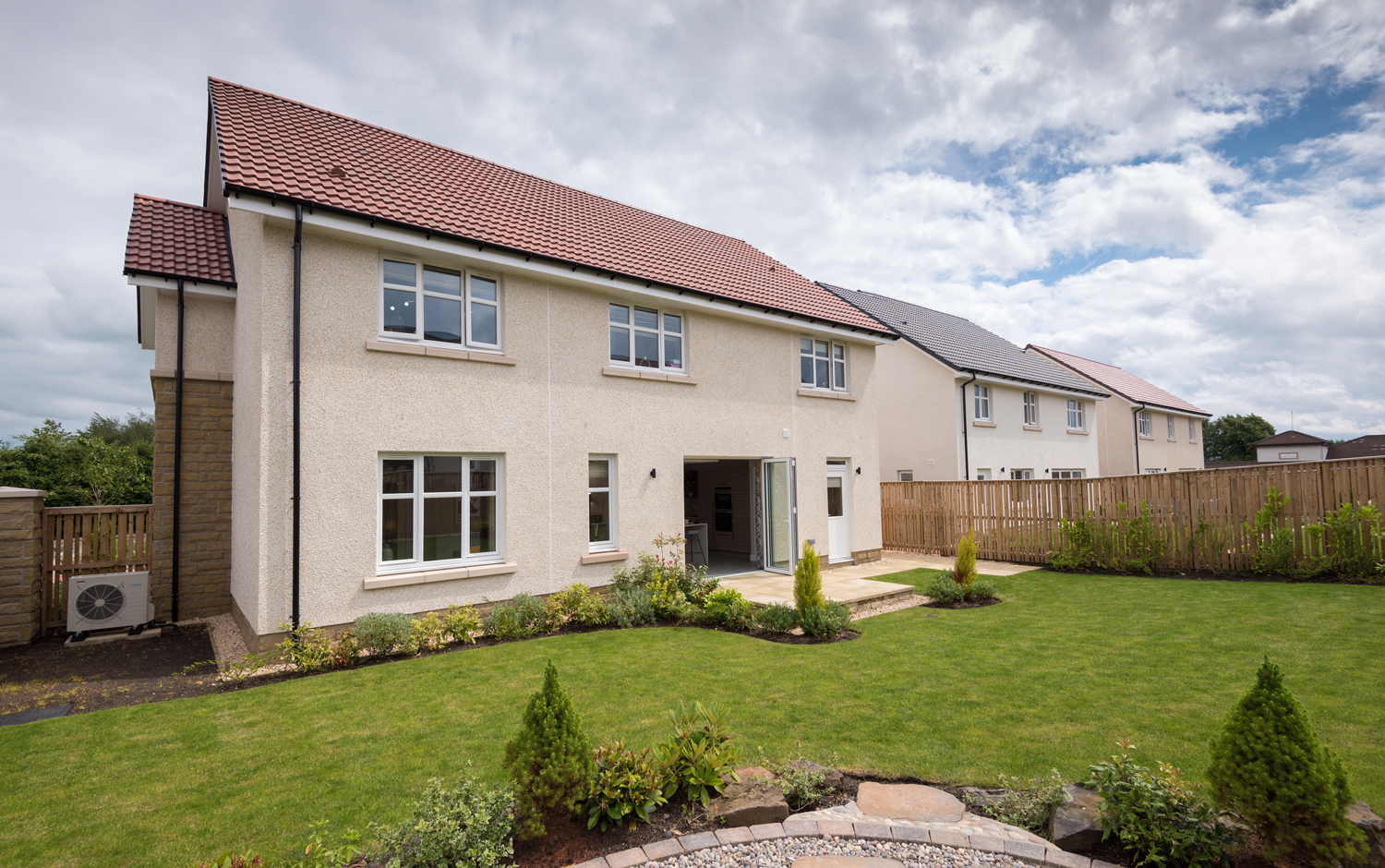 Wide view of a garden of a modern house with open bifold doors leading into a kitchen